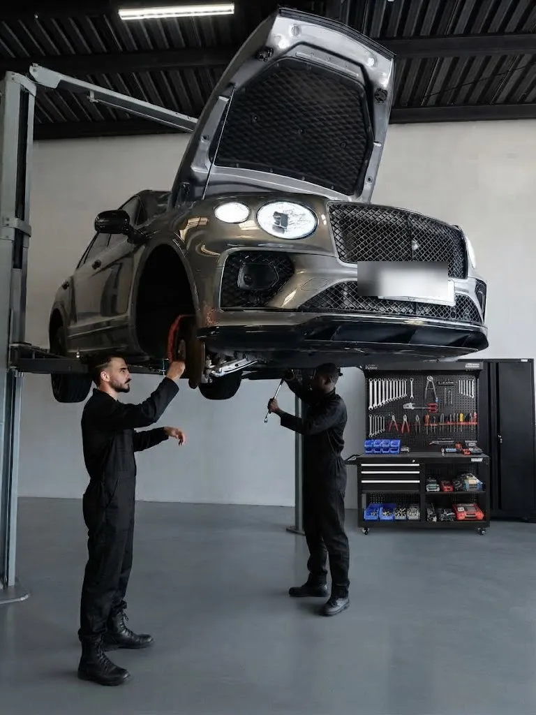 A Bentley Bentayga raised on a two-post lift while two technicians work underneath it