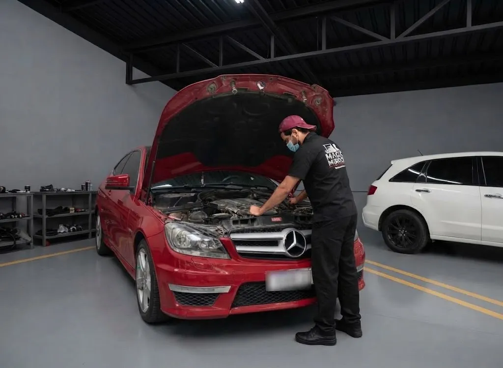 A red Mercedes C-Class with its bonnet open while a technician works on the engine