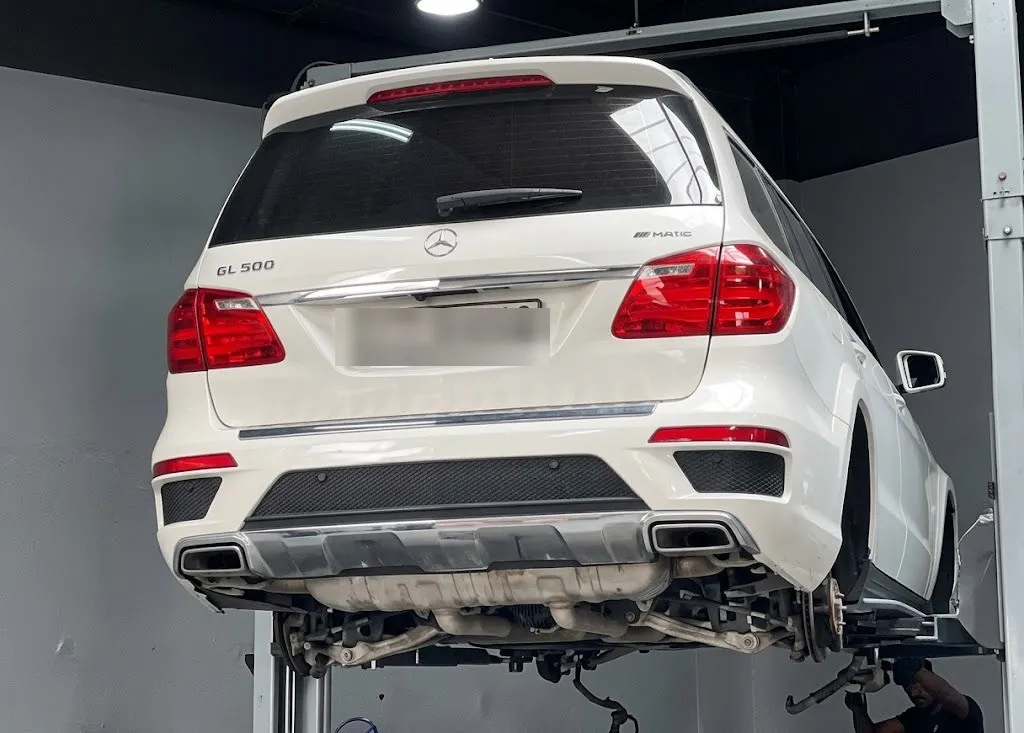 A white Mercedes GL 500 raised high on a two-post lift for underbody work
