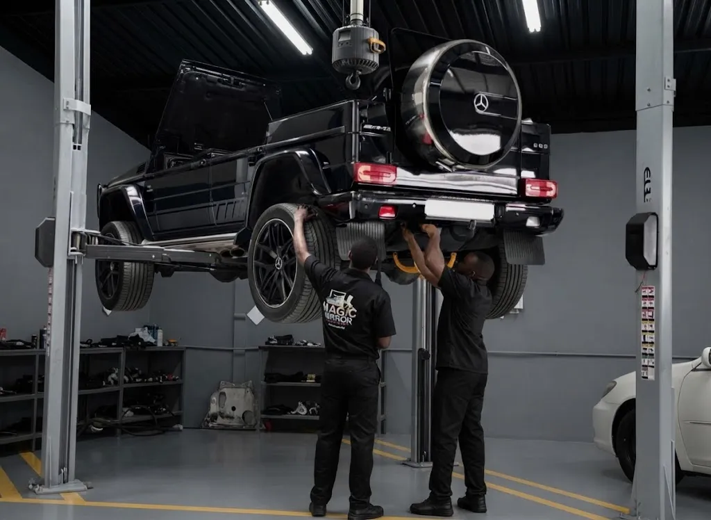 A black Mercedes G-Class raised on a two-post lift with two technicians underneath