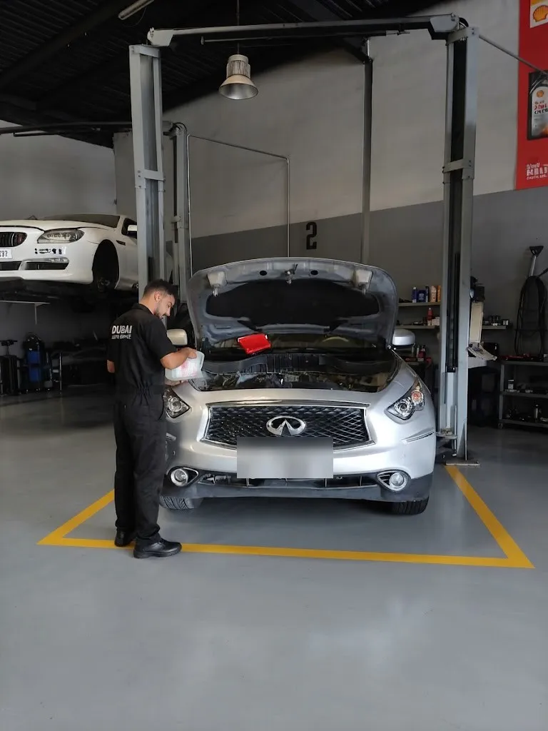 A silver Infiniti FX with its bonnet open while a technician works on the engine